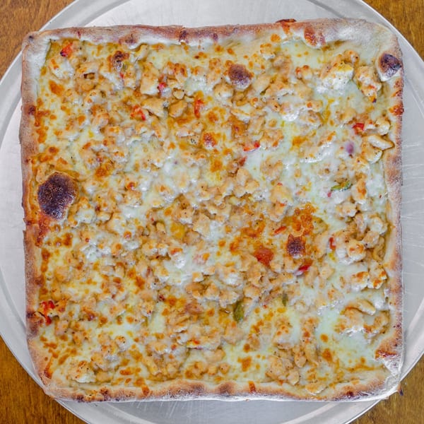 A square Catania's Pizza with white cheese and chicken pieces on a metal tray.