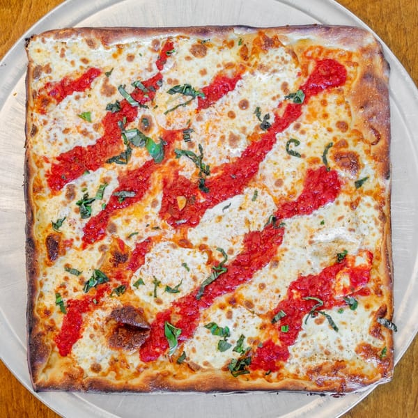 Square Catania's Pizza with red sauce stripes, melted cheese, and basil on a metal tray.