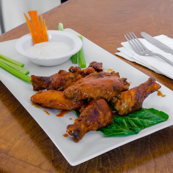 Catania's Pizza's buffalo wings with celery sticks, carrot slices, and ranch dressing on a white plate.